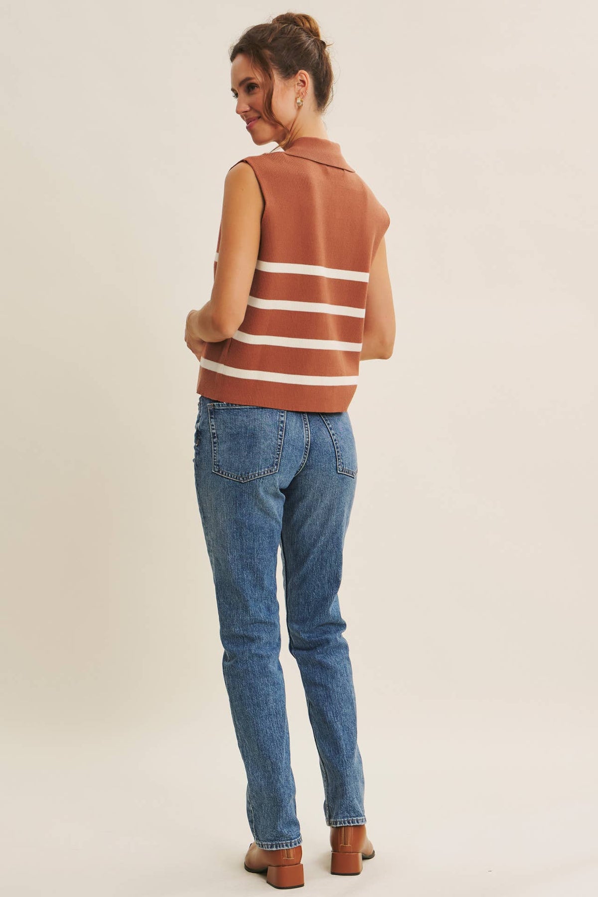 Woman wearing a brown sleeveless striped top and blue jeans on a beige background