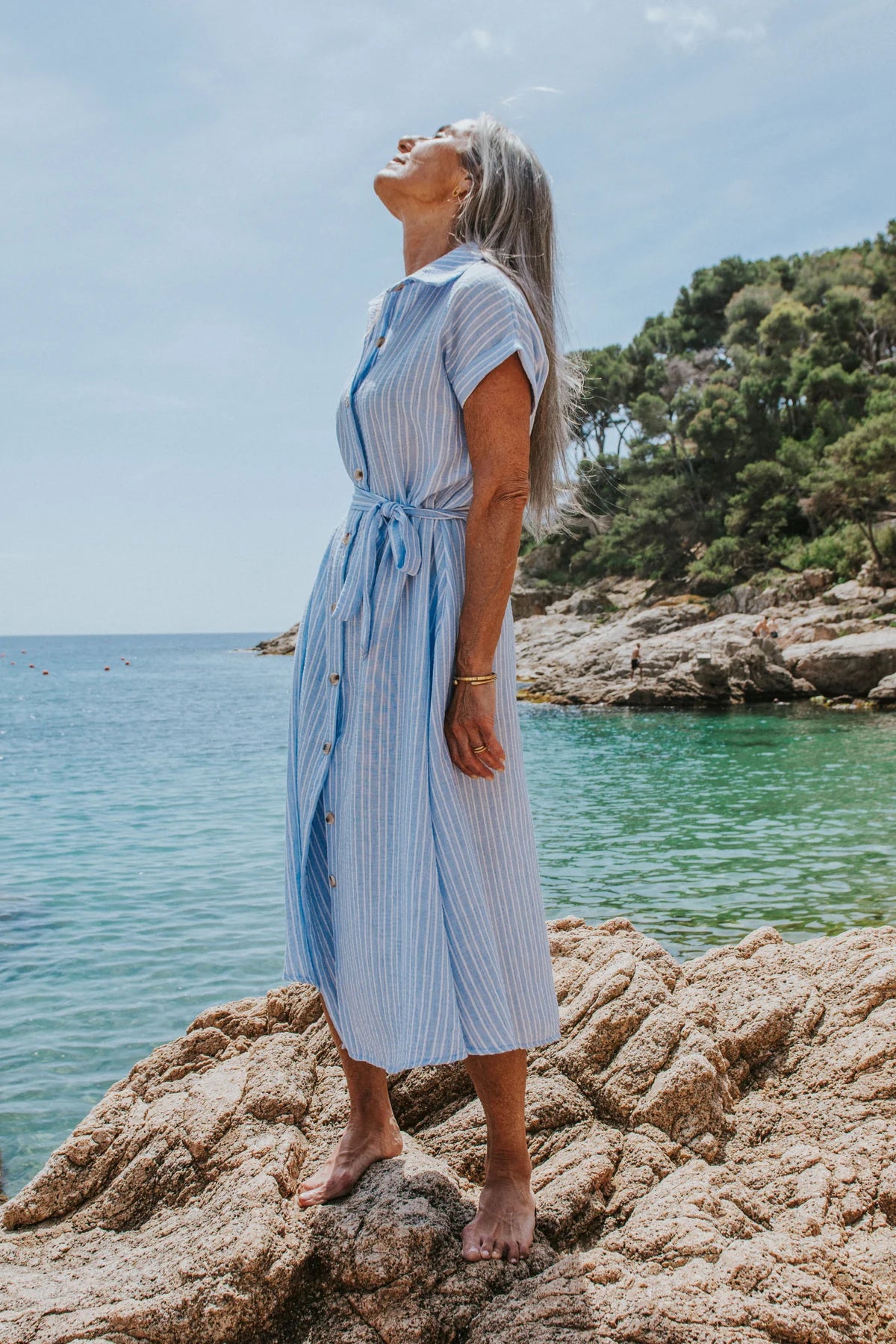 Woman in a blue striped dress standing on rocks by the sea