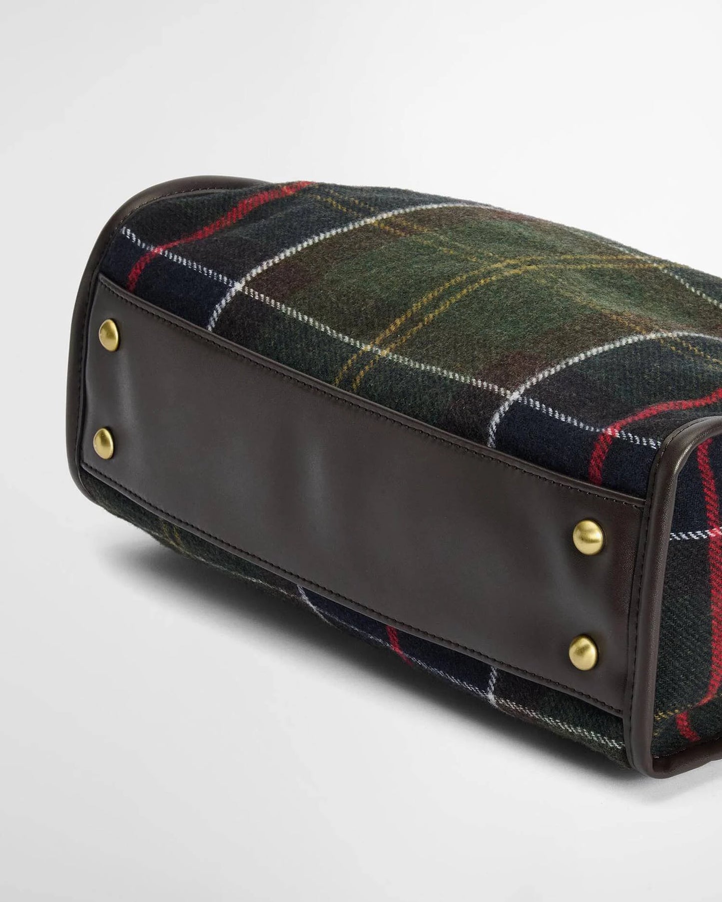 A close-up of a luxury handbag featuring a dark green and black tartan plaid wool fabric body with red and yellow stripes, finished with a smooth dark brown leather base and brass hardware.