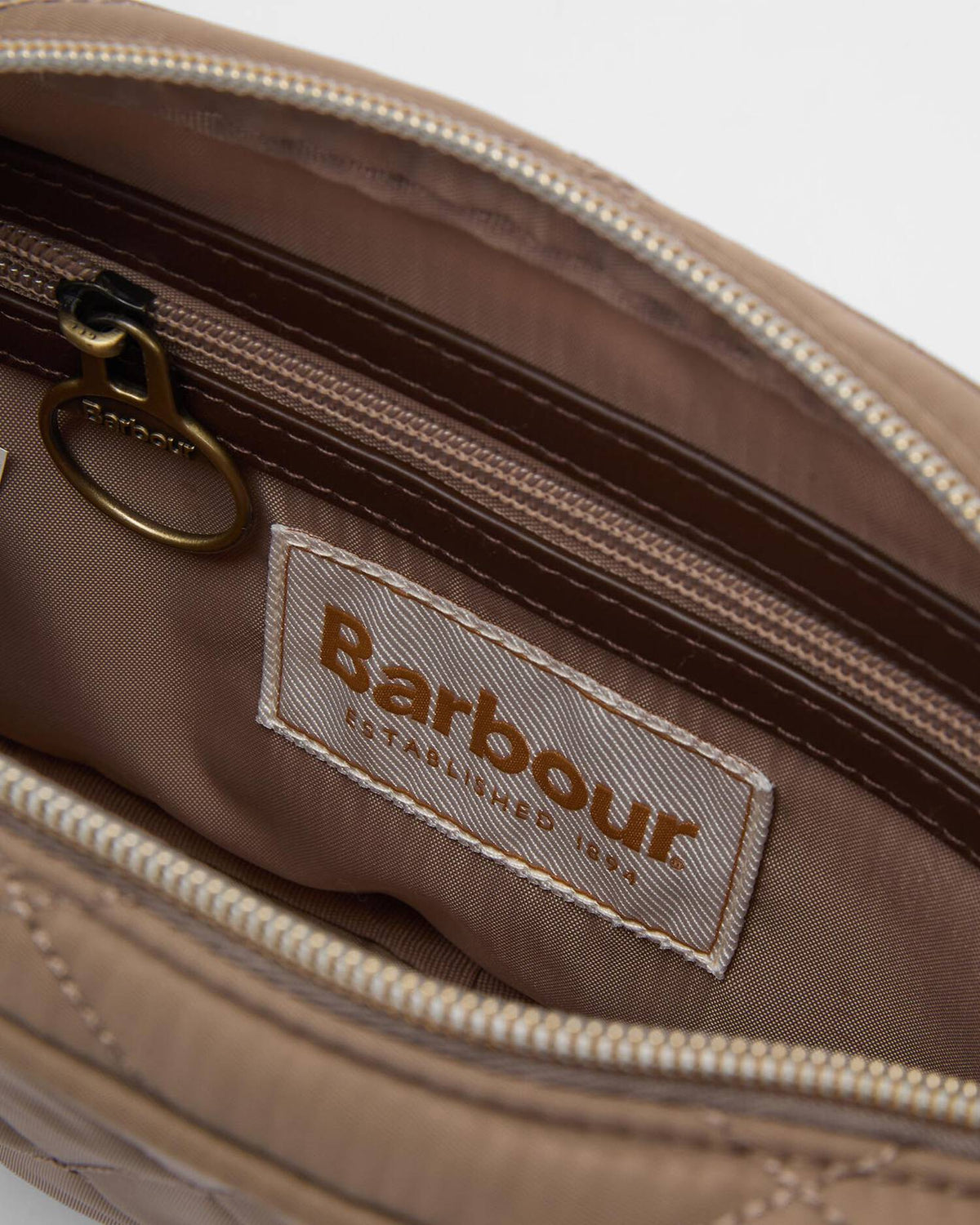 Close-up of the interior of a Barbour pouch or bag, showing a tan quilted exterior, a brown zipper track, and a sewn-on Barbour brand label on the inside.