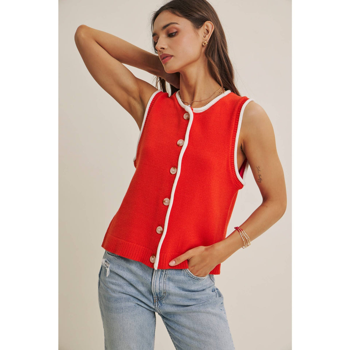 Woman wearing a red sleeveless cardigan with white trim against a neutral background