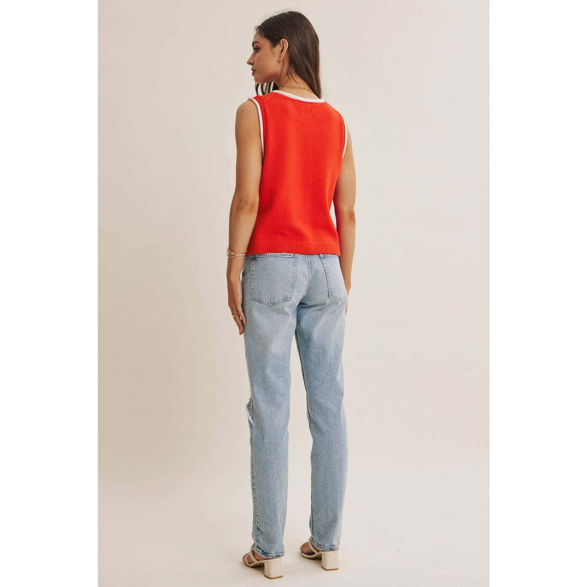 Woman wearing a red sleeveless top and light blue jeans on a plain background
