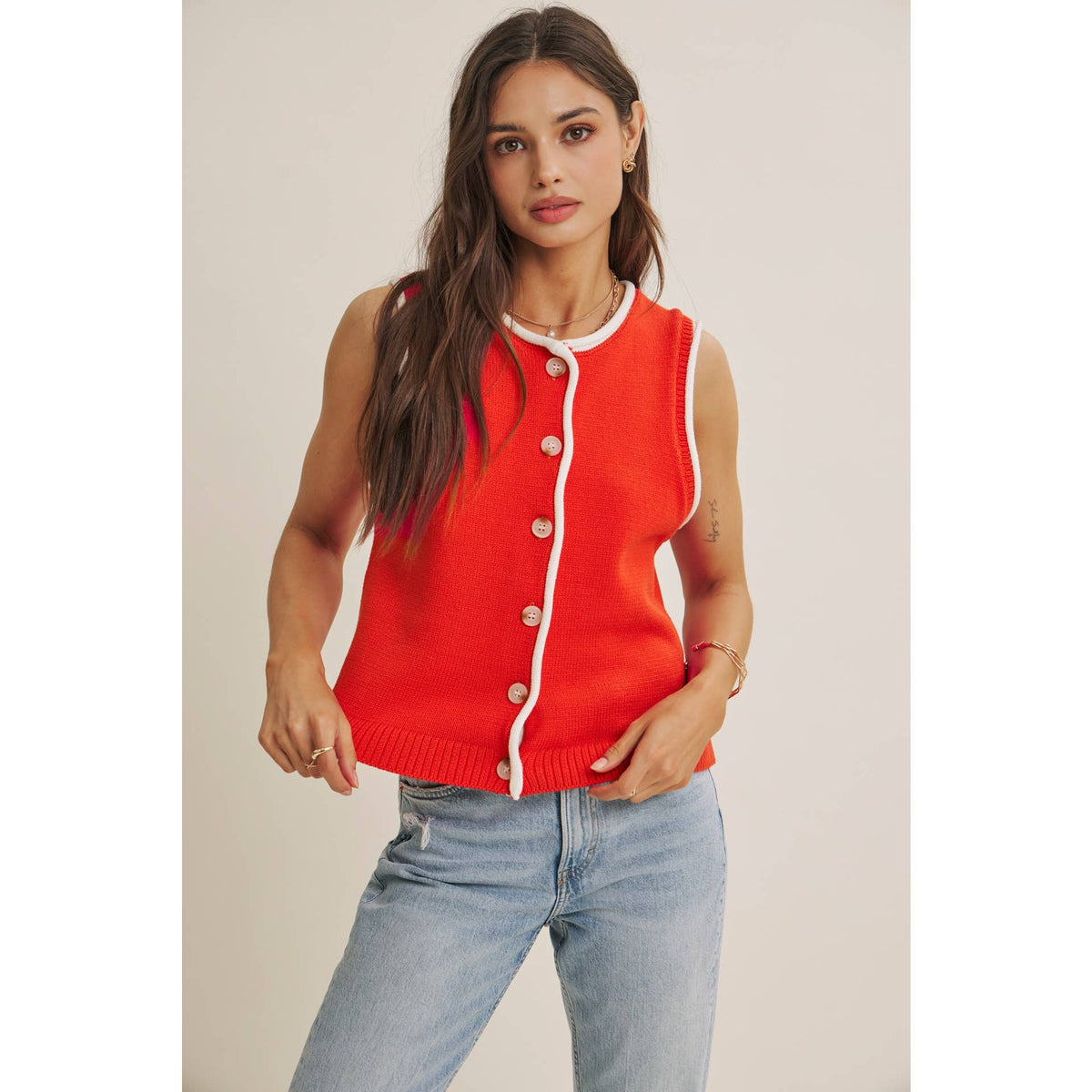 Woman wearing a red sleeveless button-up top with light blue jeans on a plain background