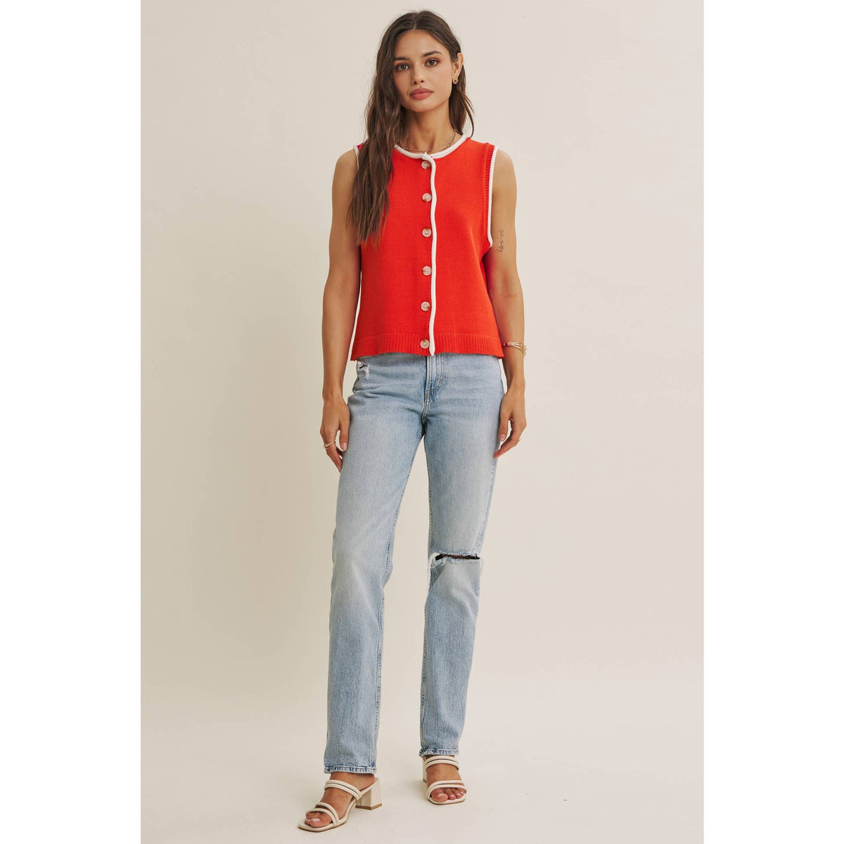 Woman wearing a red sleeveless top with white buttons and light blue jeans on a beige background