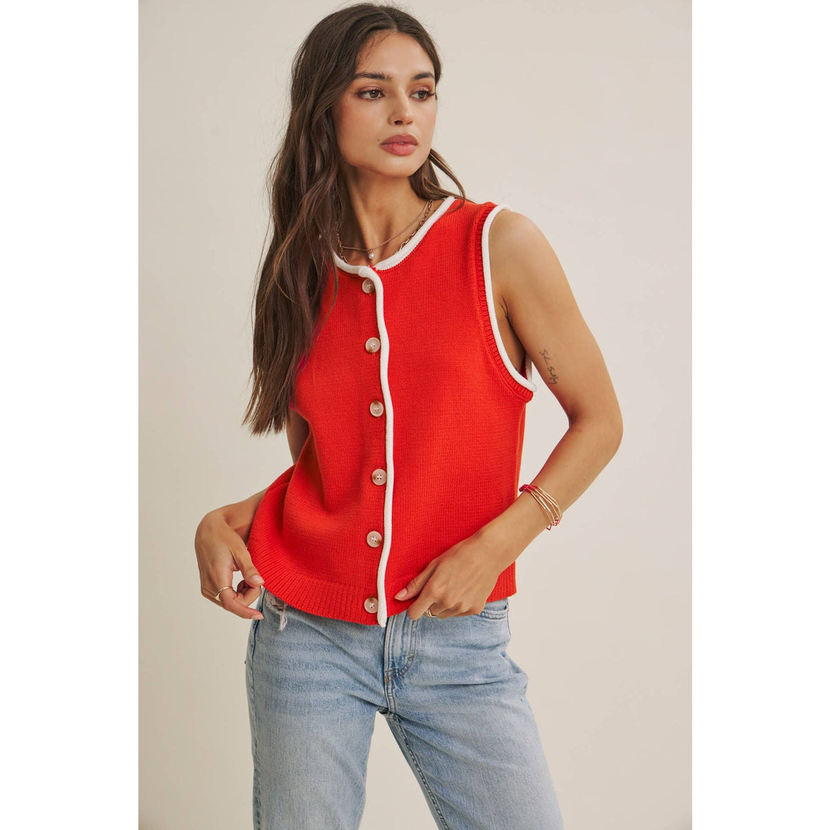 Woman wearing a red sleeveless sweater with white buttons against a plain background