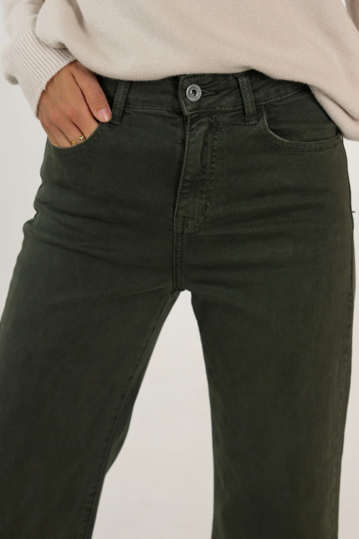 Person wearing dark green jeans with a plain background