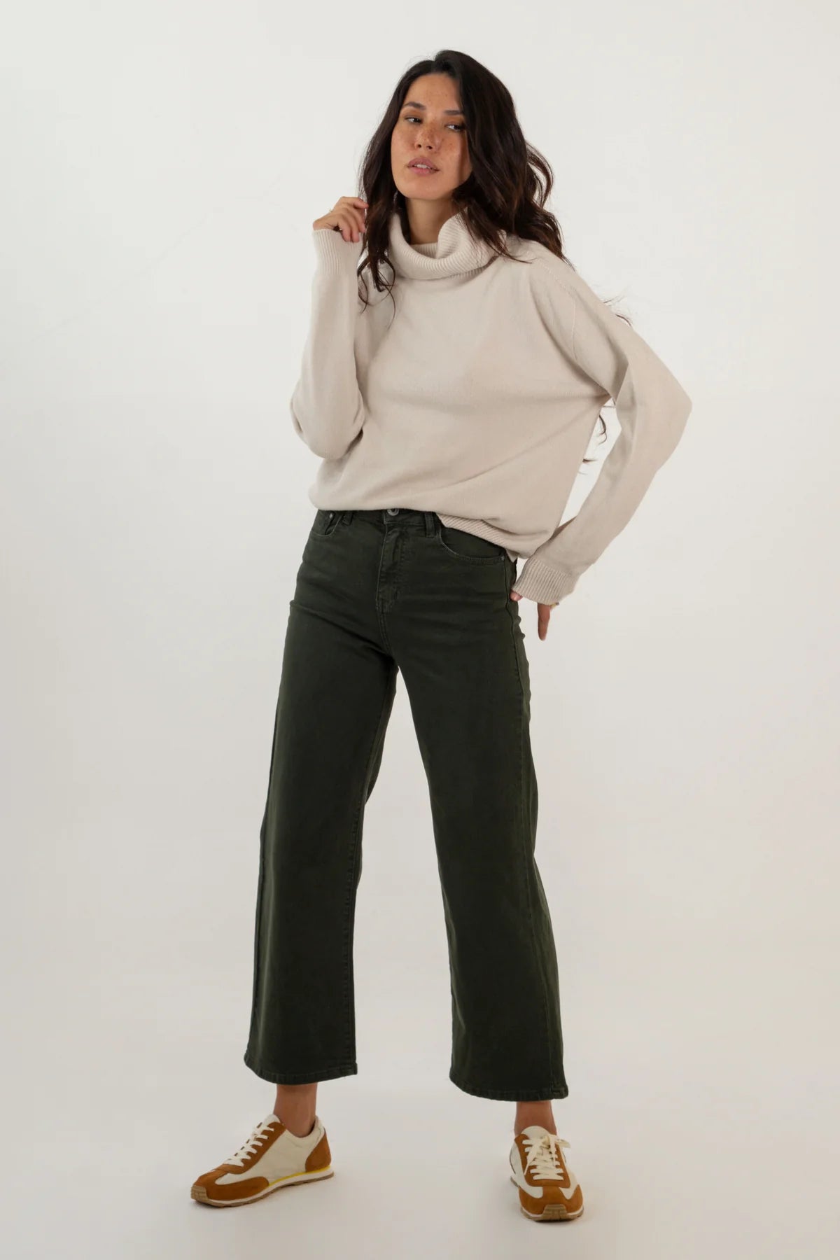 Woman wearing a beige sweater and dark green pants on a white background