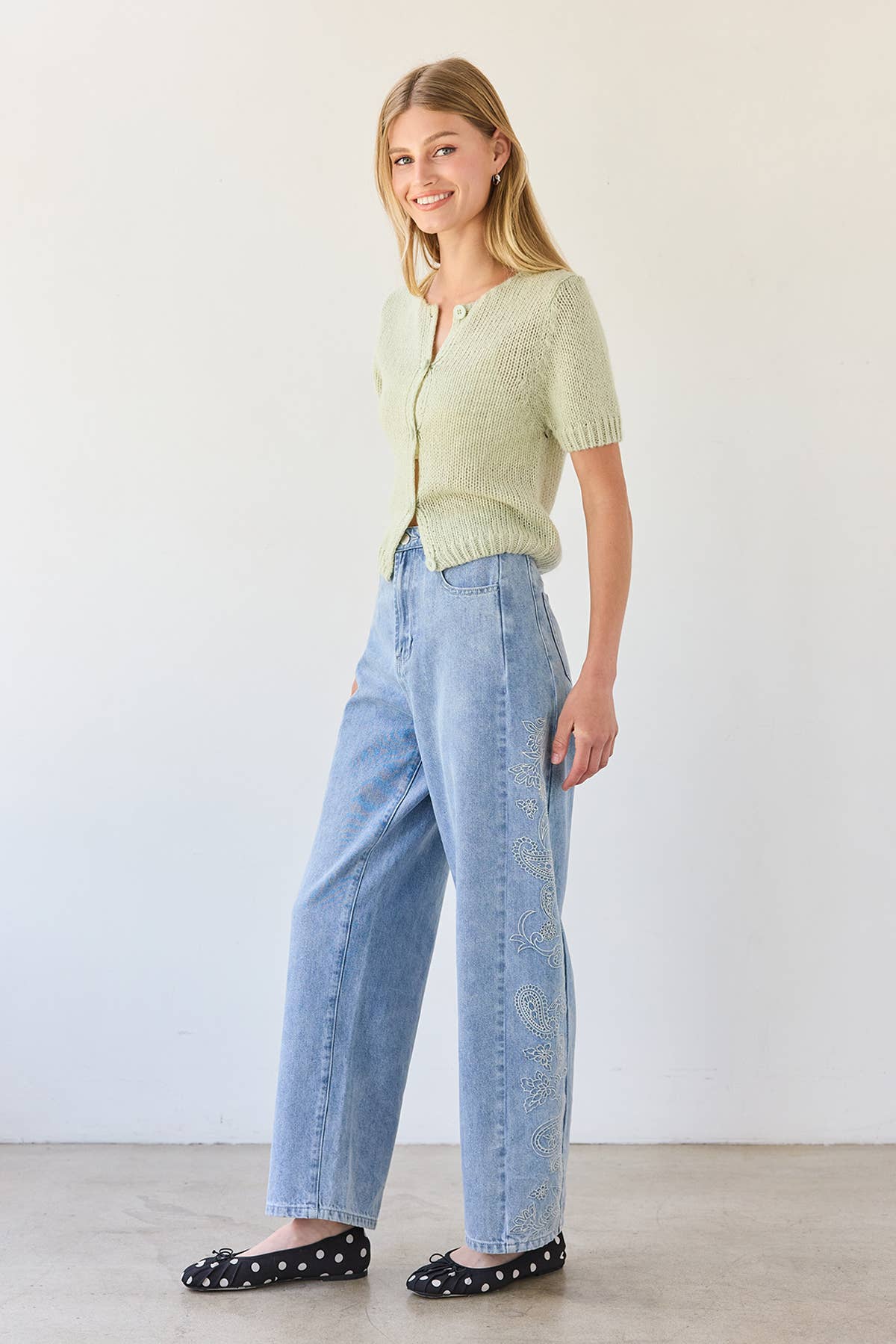 Woman wearing a light green cardigan and blue jeans against a white background