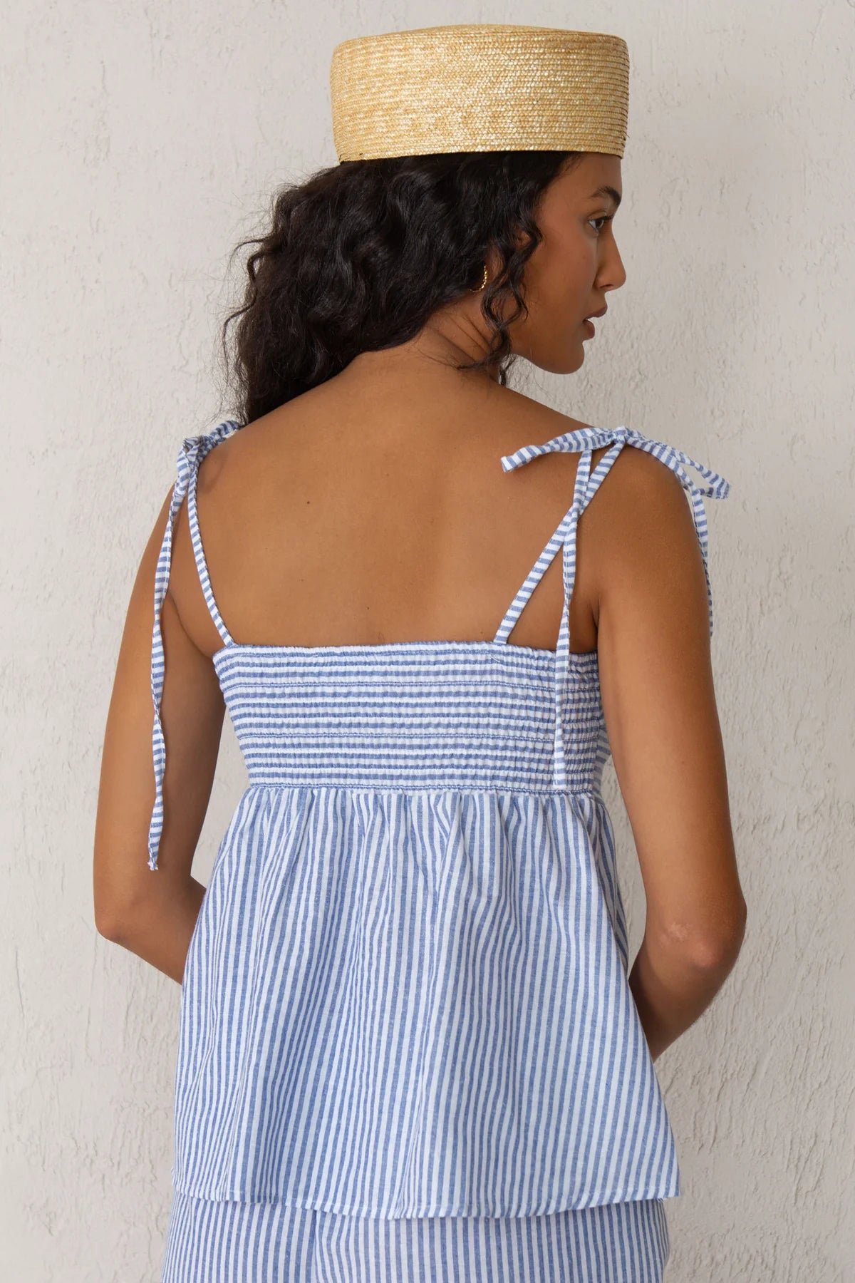 Woman wearing a blue and white striped tank top with a straw hat against a plain background