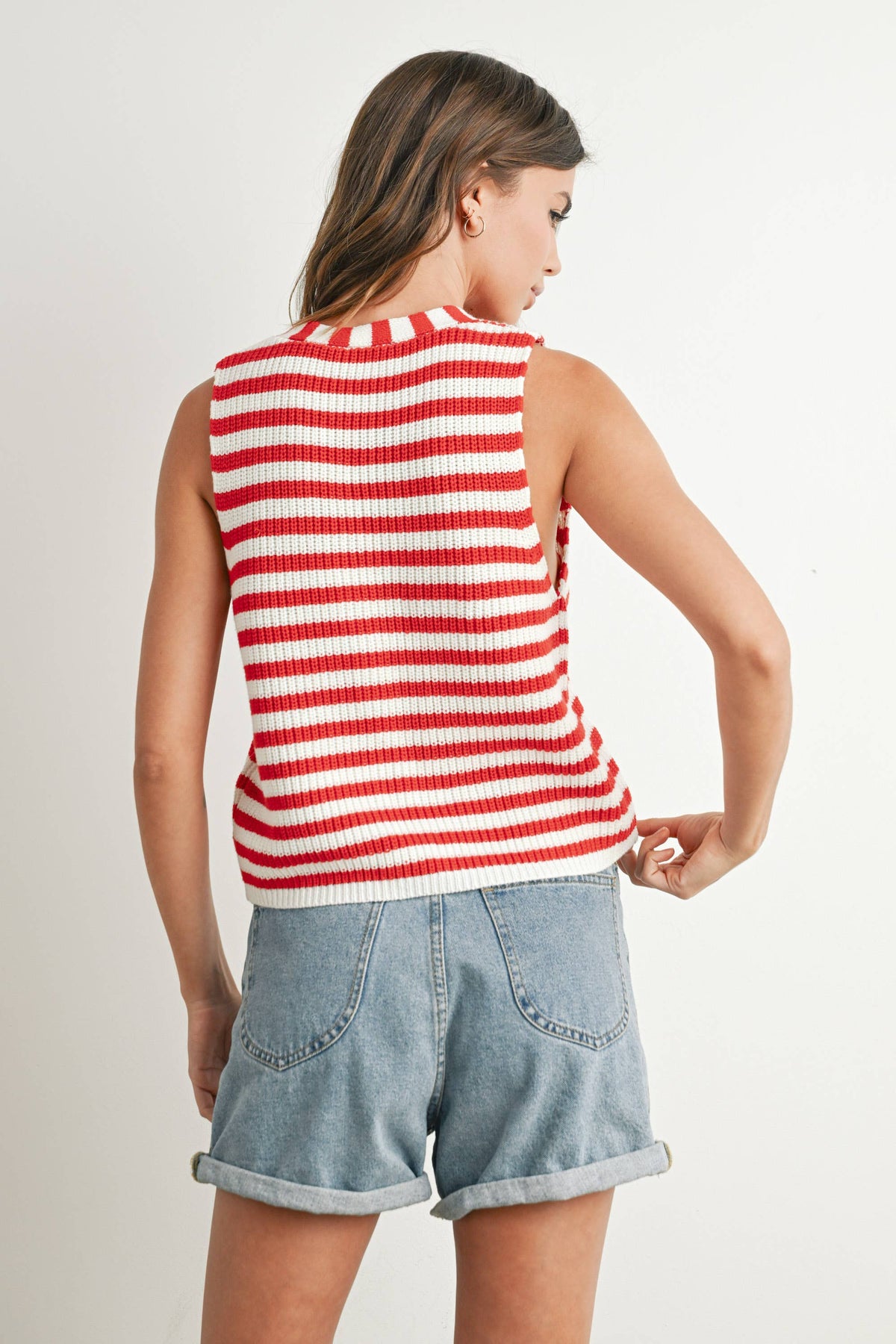 Woman wearing a red and white striped sleeveless top and denim shorts on a plain background