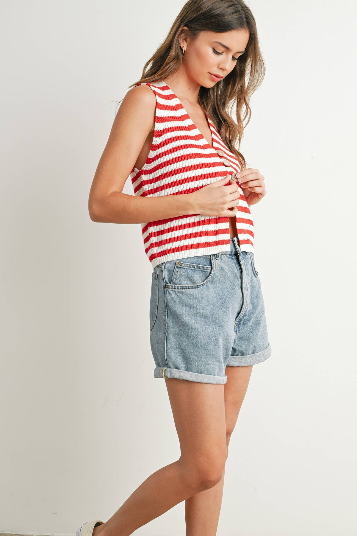 Woman wearing a red and white striped tank top and denim shorts on a plain background