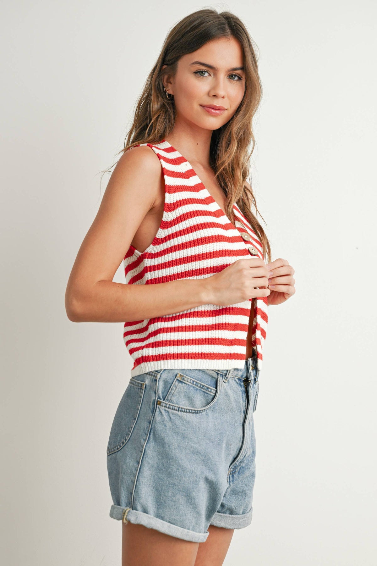 Woman wearing a red and white striped tank top and denim shorts on a plain background