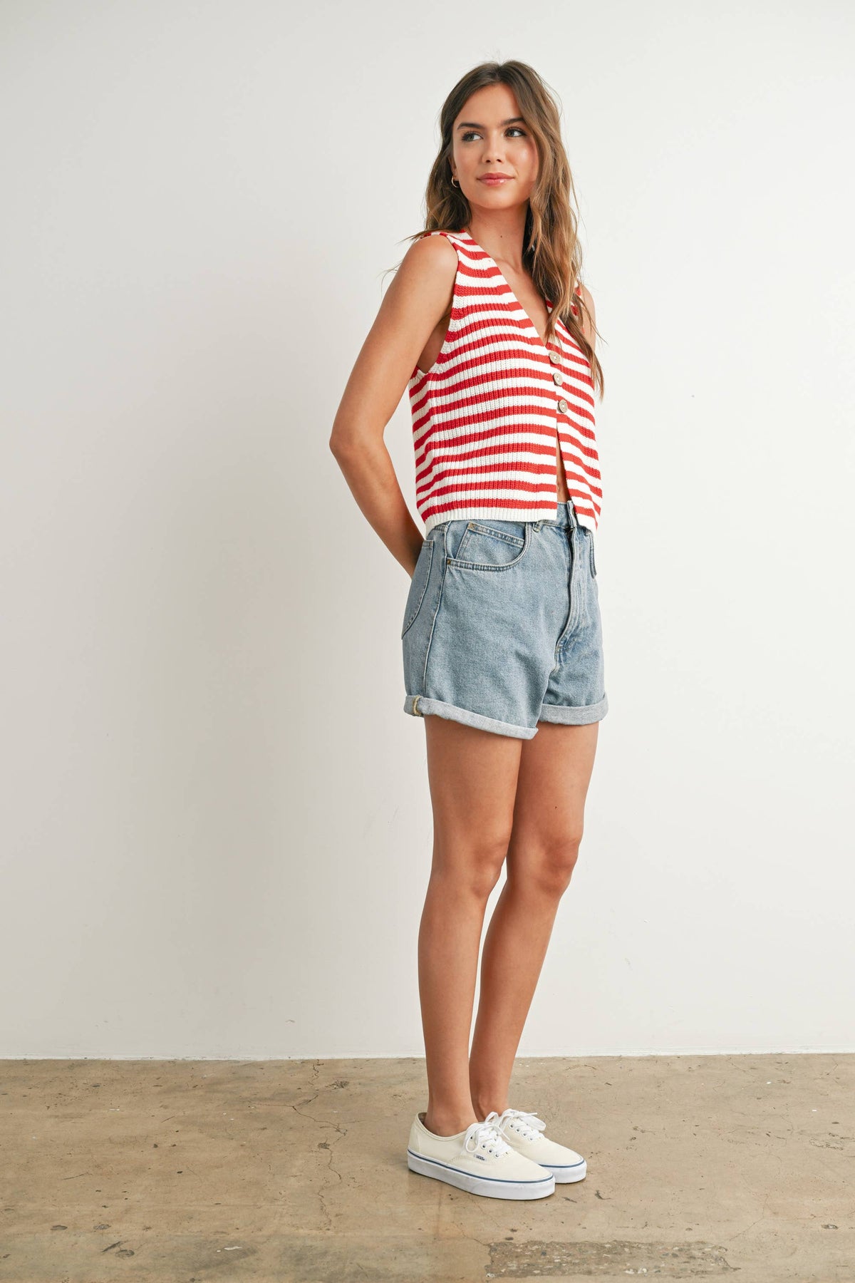 Woman wearing a red and white striped tank top and denim shorts against a plain background