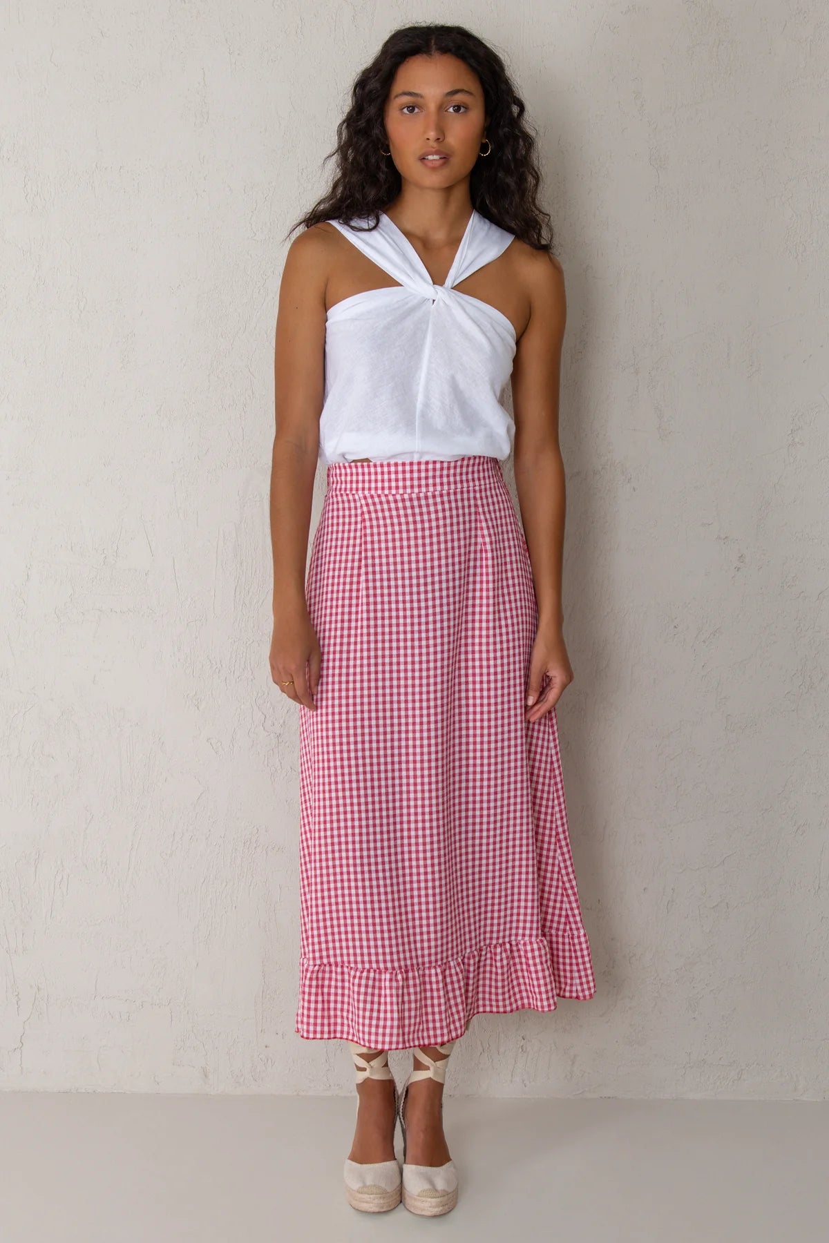 Woman wearing a white top and red checkered skirt against a plain background