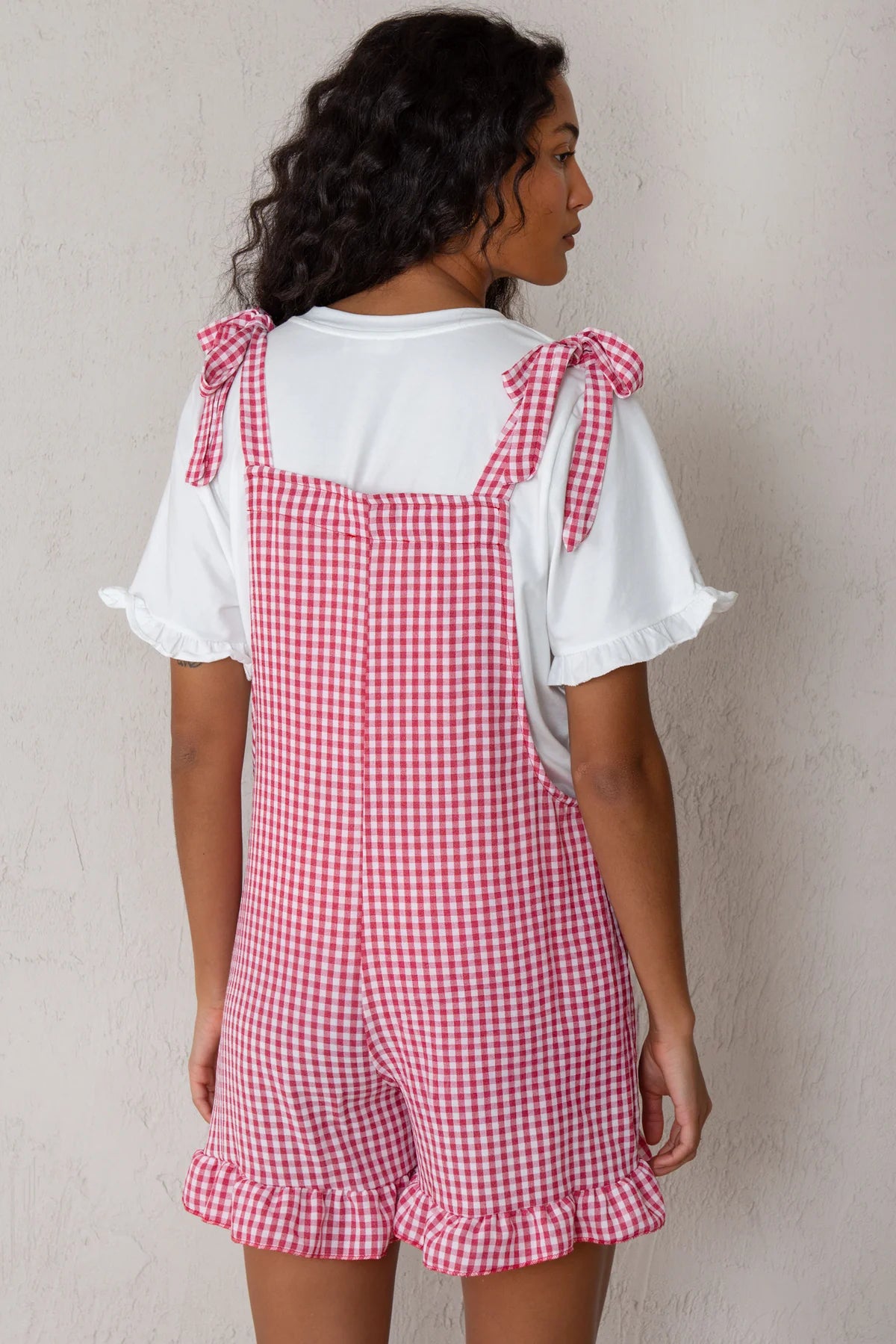 Person wearing a red and white checkered dress over a white shirt against a plain background