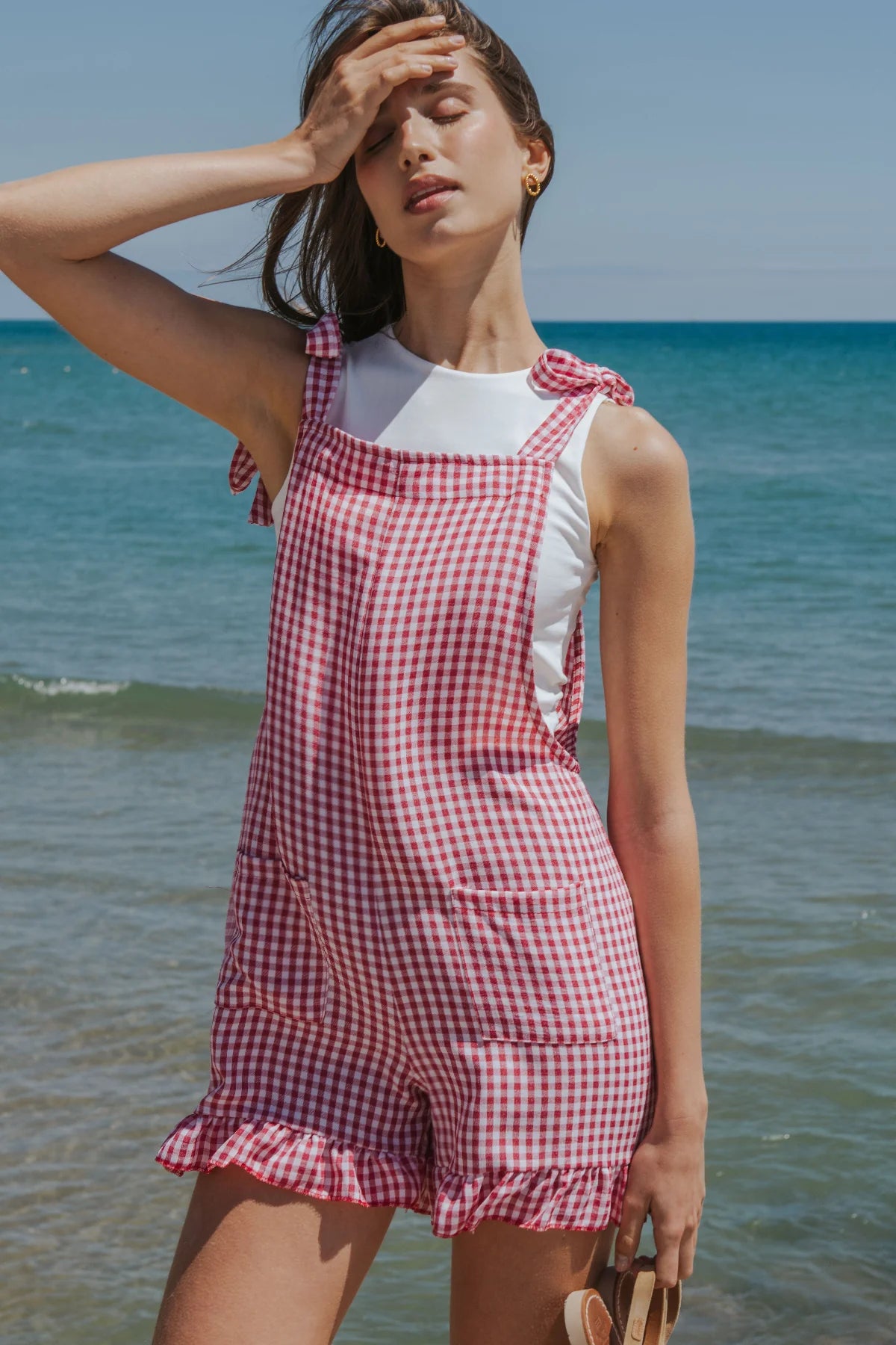 Woman wearing a red and white checkered dress standing on a beach.