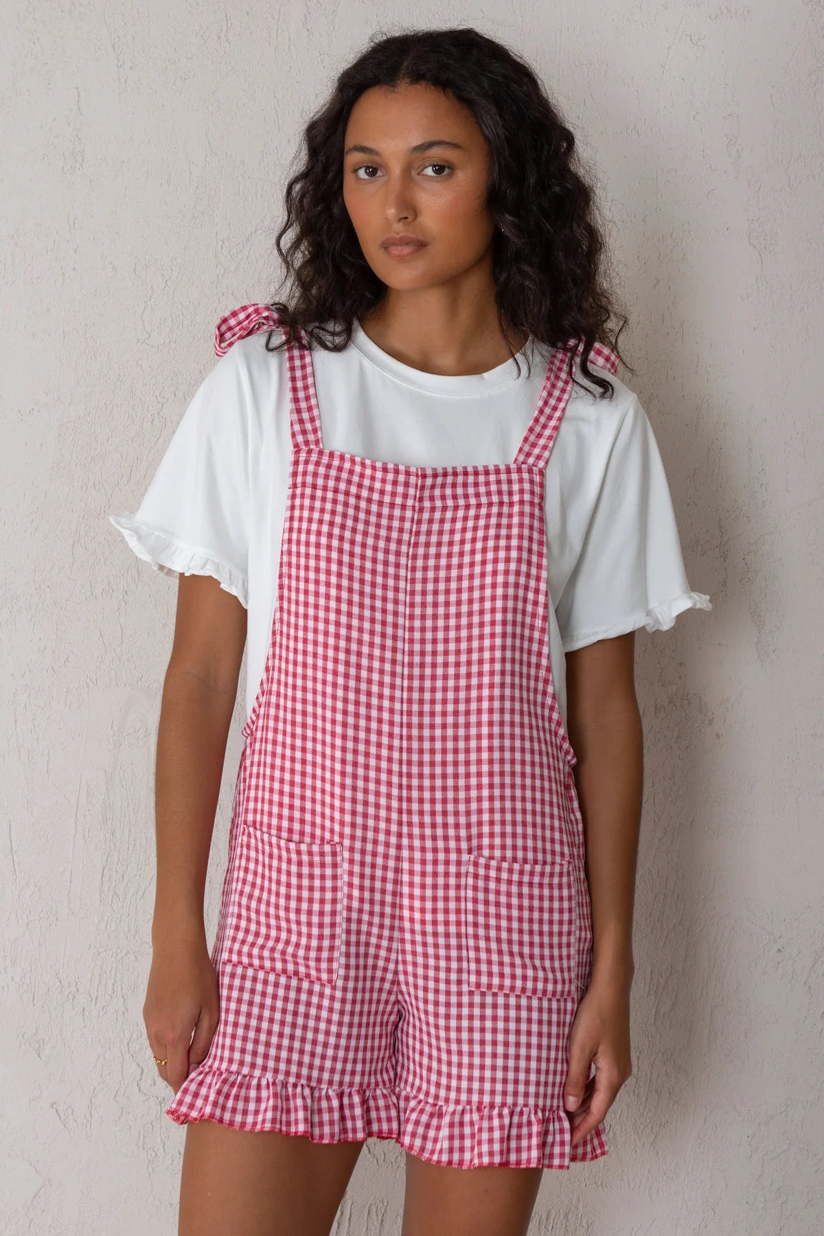 Woman wearing a red and white checkered pinafore over a white shirt against a plain background