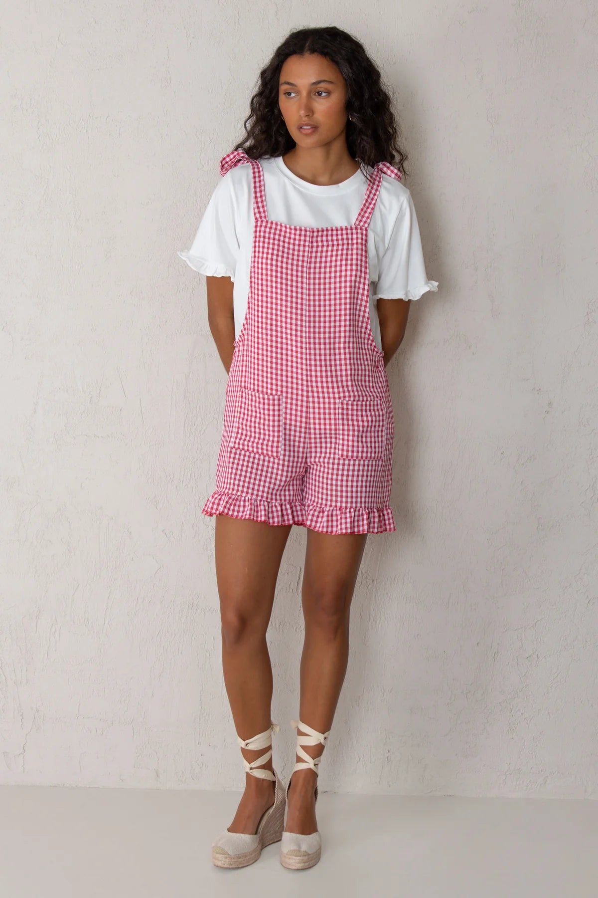 Woman wearing a red and white checkered dress over a white t-shirt against a plain background