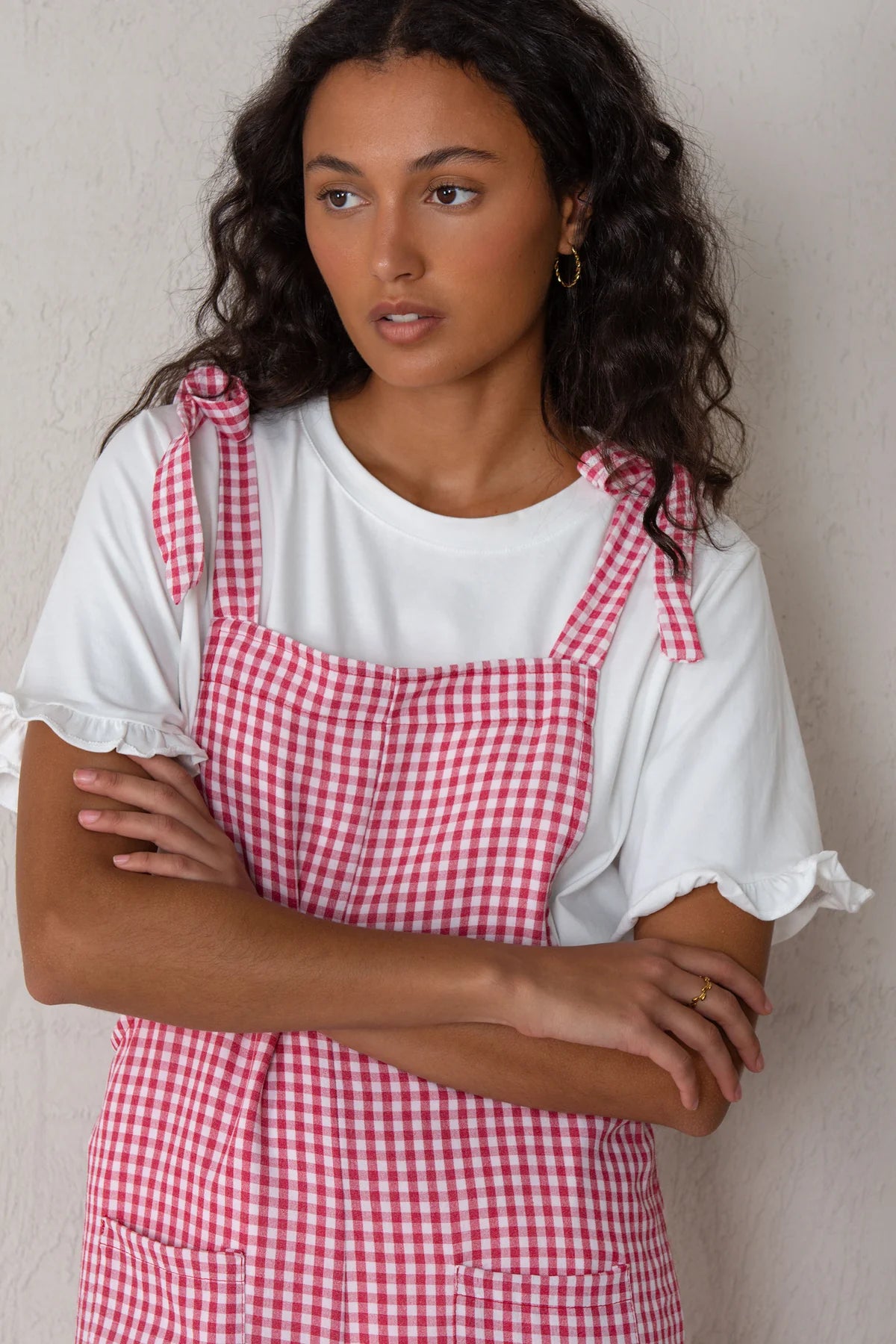 Woman wearing a red and white checkered apron over a white shirt against a plain background