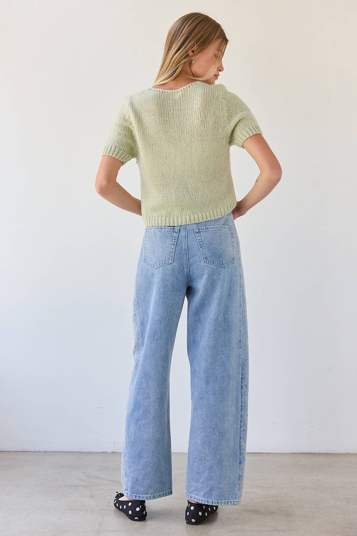 Woman wearing a light green sweater and blue jeans against a white background