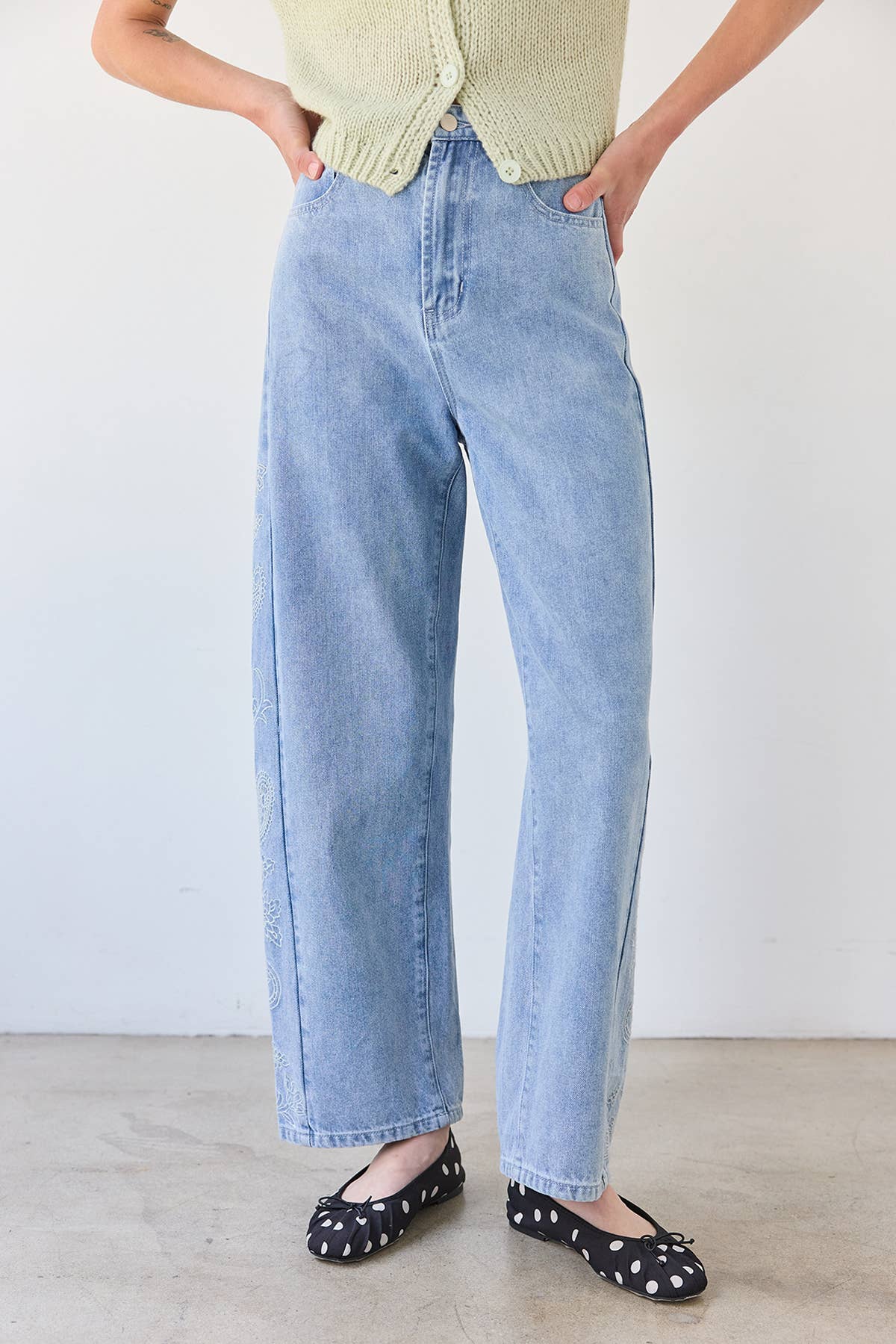 Person wearing light blue jeans and polka dot shoes on a plain background