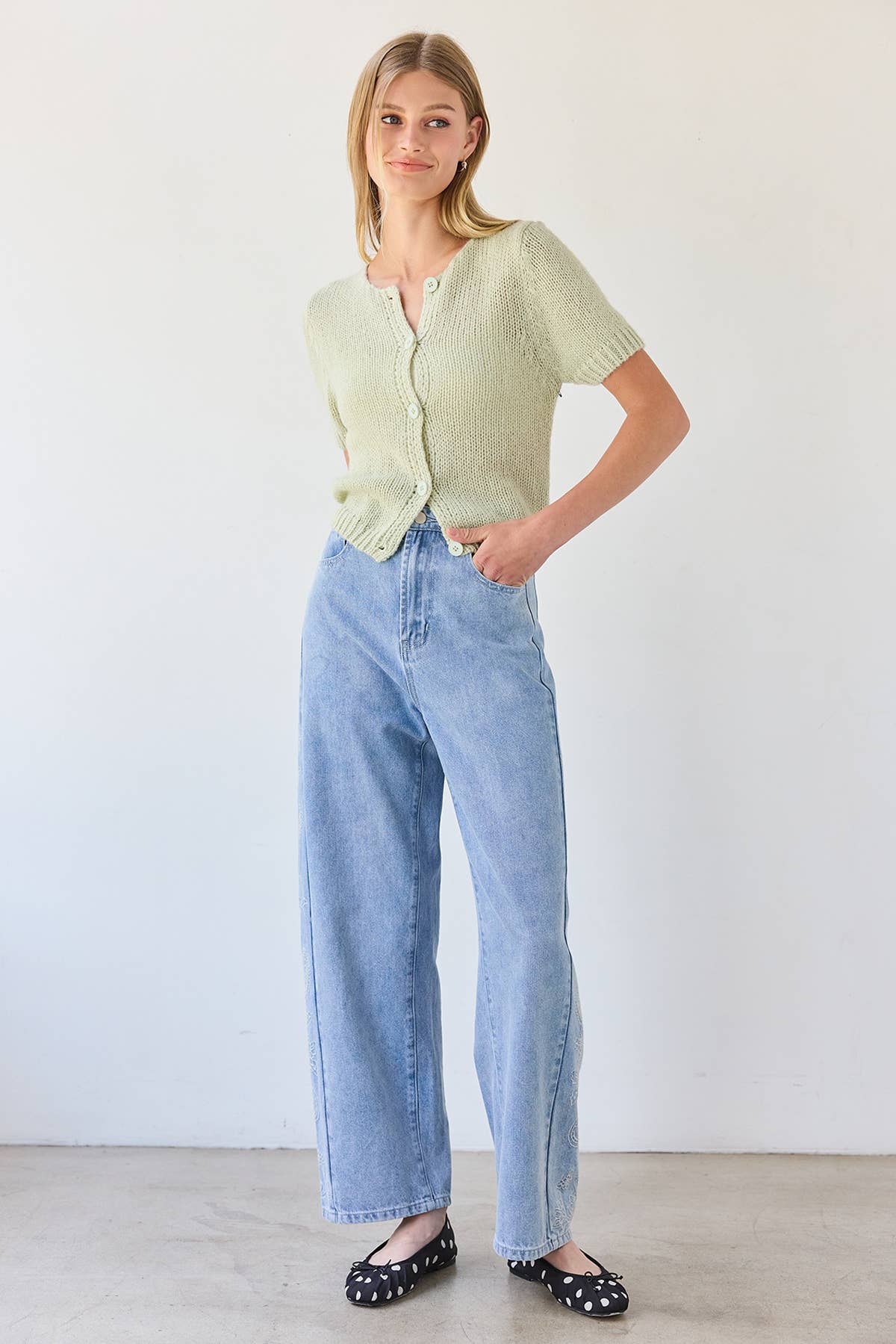 Woman wearing a light green cardigan and blue jeans against a white background