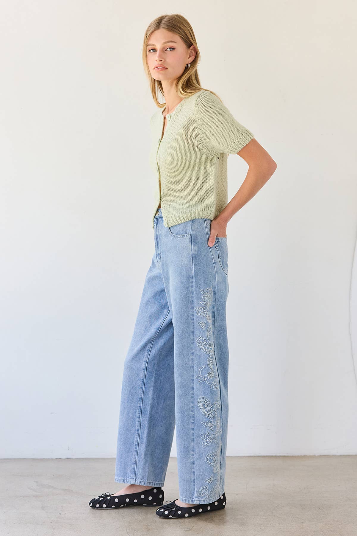 Woman wearing a light green sweater and blue jeans against a white background