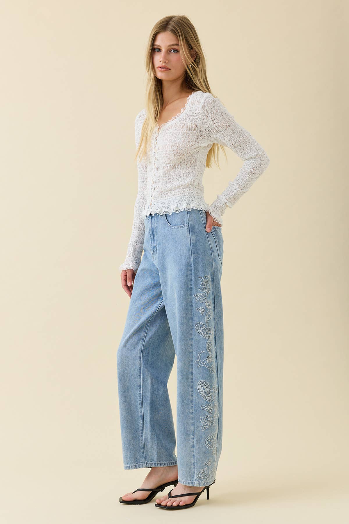 Woman wearing a white lace top and light blue jeans on a beige background