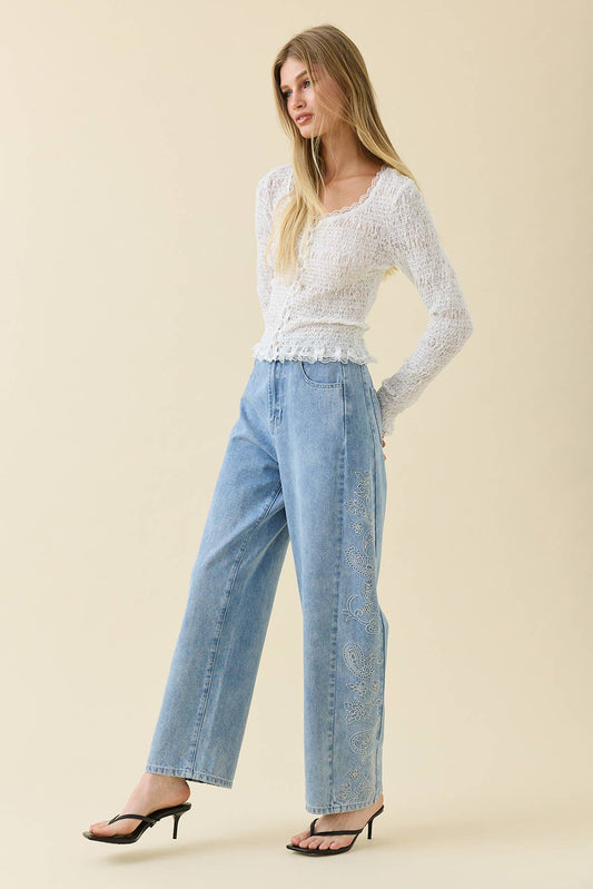 Woman wearing a white lace top and light blue jeans on a beige background