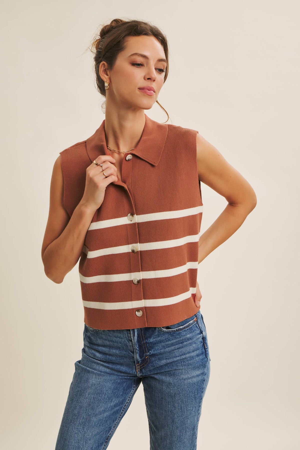 Woman wearing a brown and white striped vest with blue jeans on a plain background