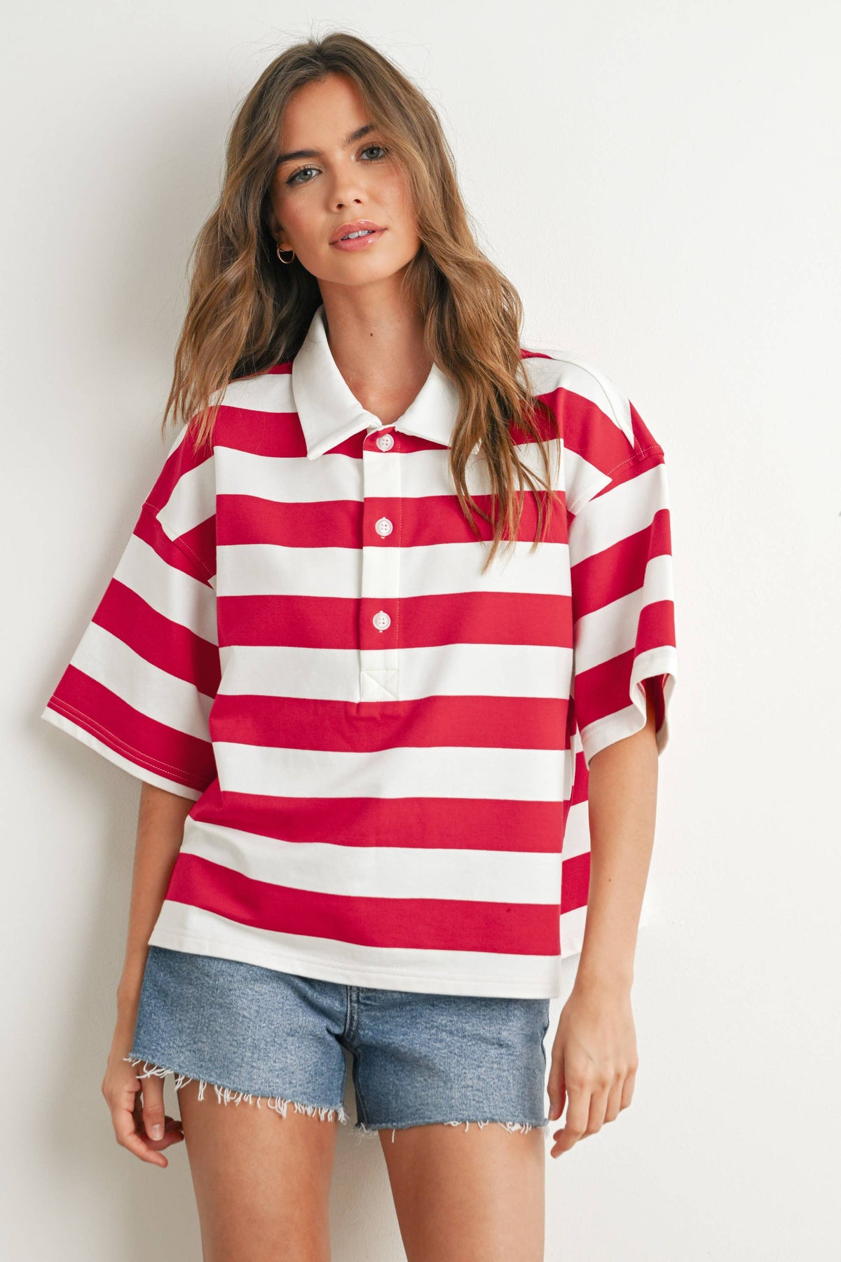 Woman wearing a red and white striped shirt with denim shorts on a plain background