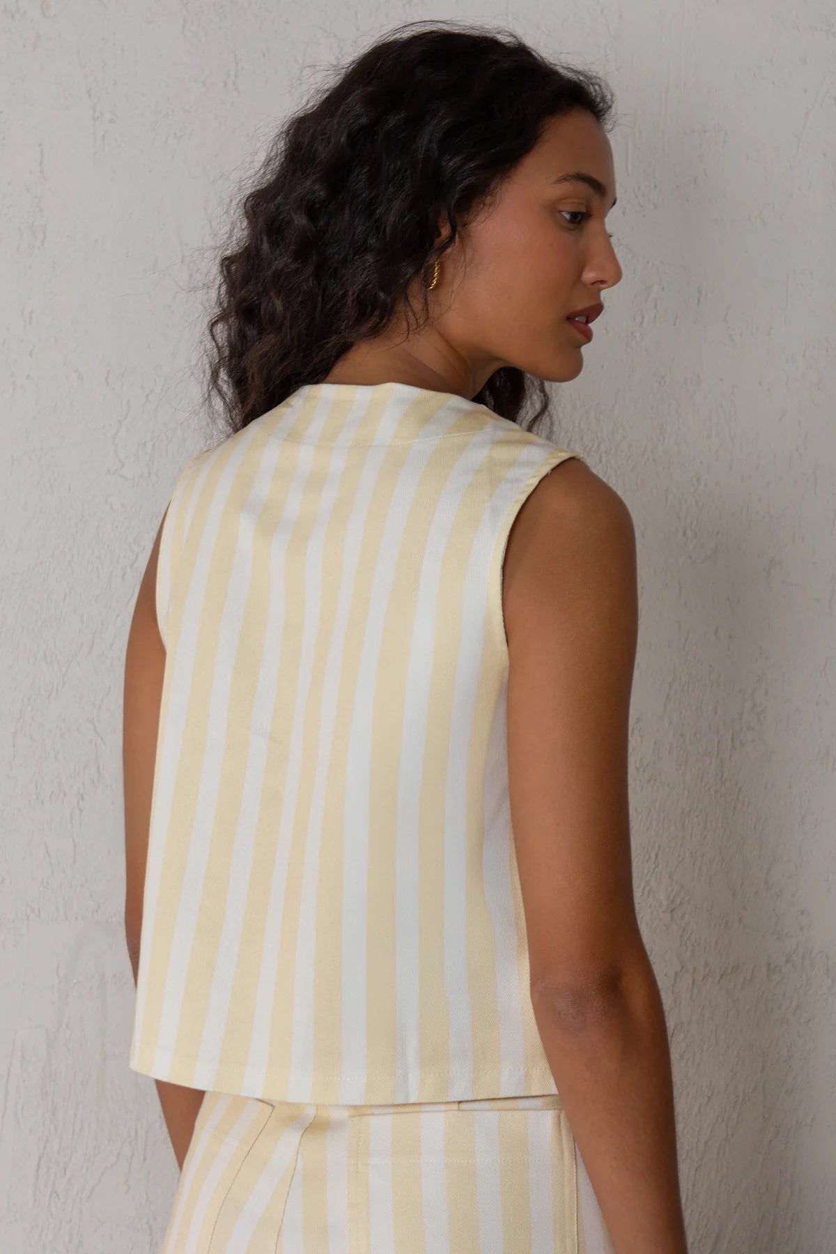 Woman wearing a yellow and white striped sleeveless top against a plain background