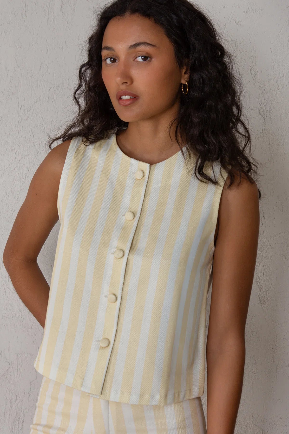Woman wearing a yellow and white striped sleeveless top against a plain background