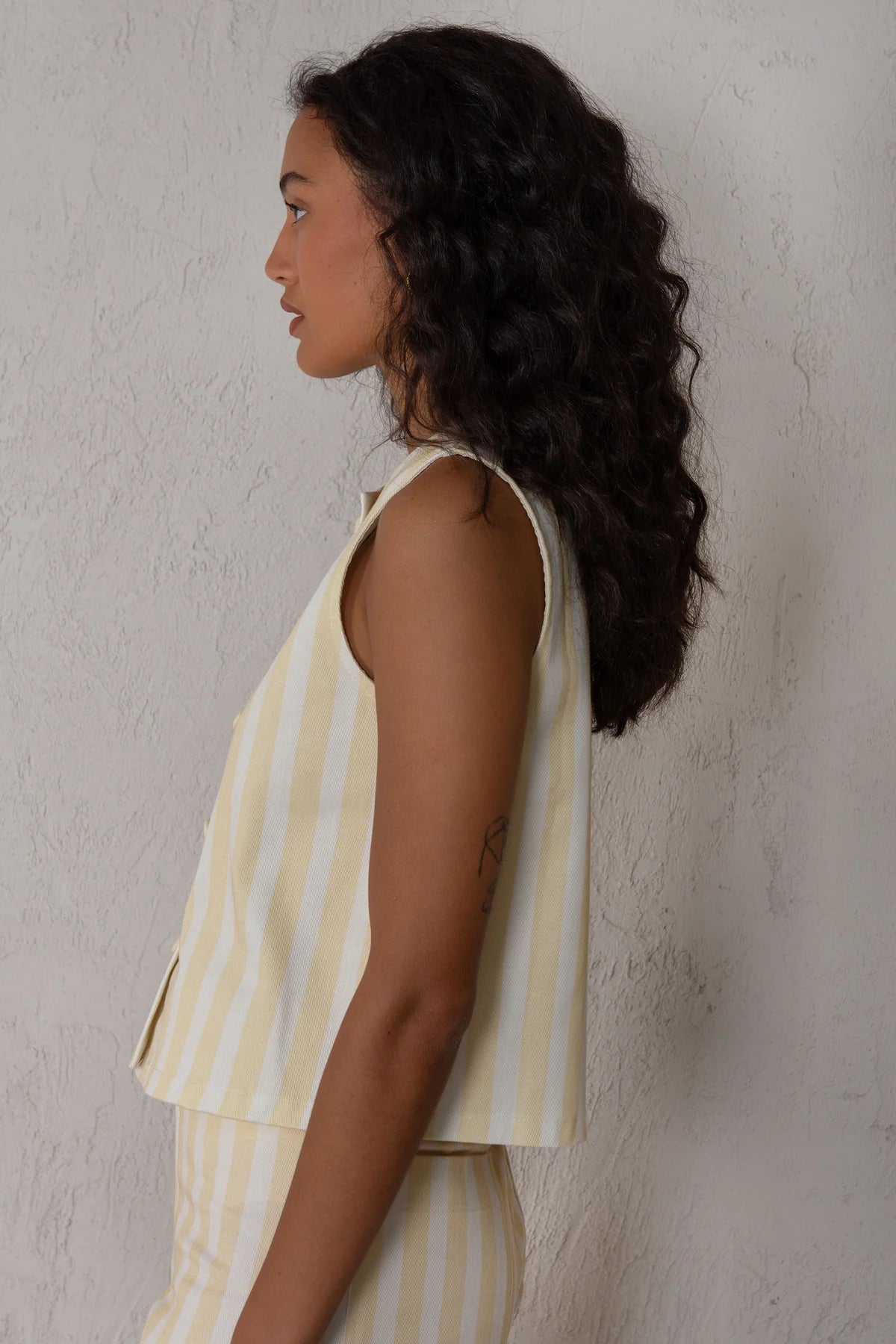 Woman wearing a yellow and white striped sleeveless top against a textured wall.