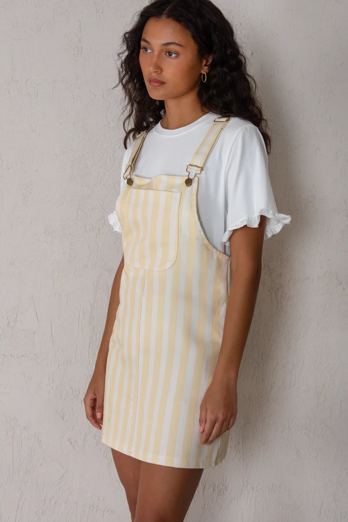 Woman wearing a yellow striped dress over a white shirt against a plain background