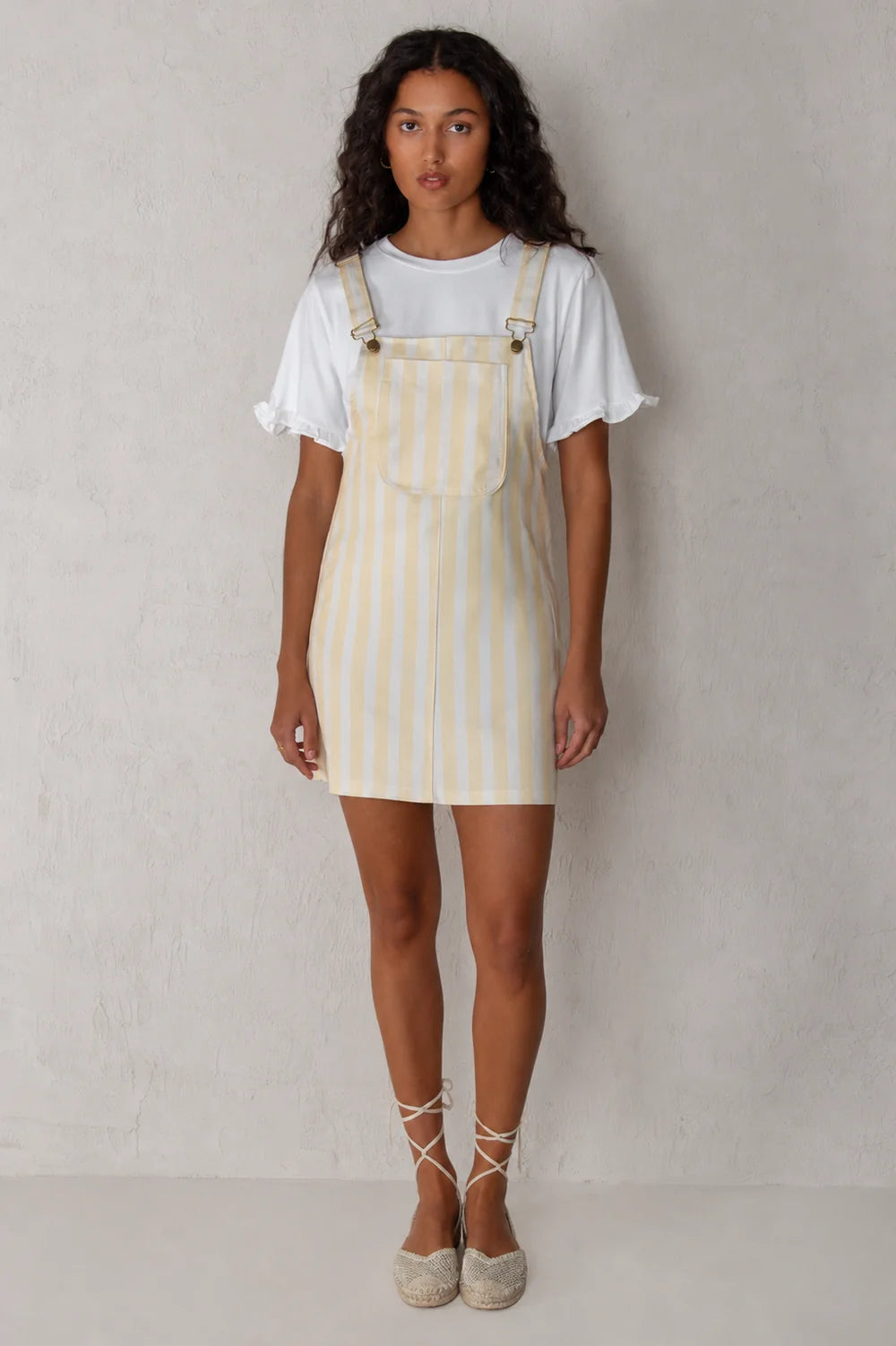 Woman wearing a yellow and white striped dress over a white t-shirt against a plain background