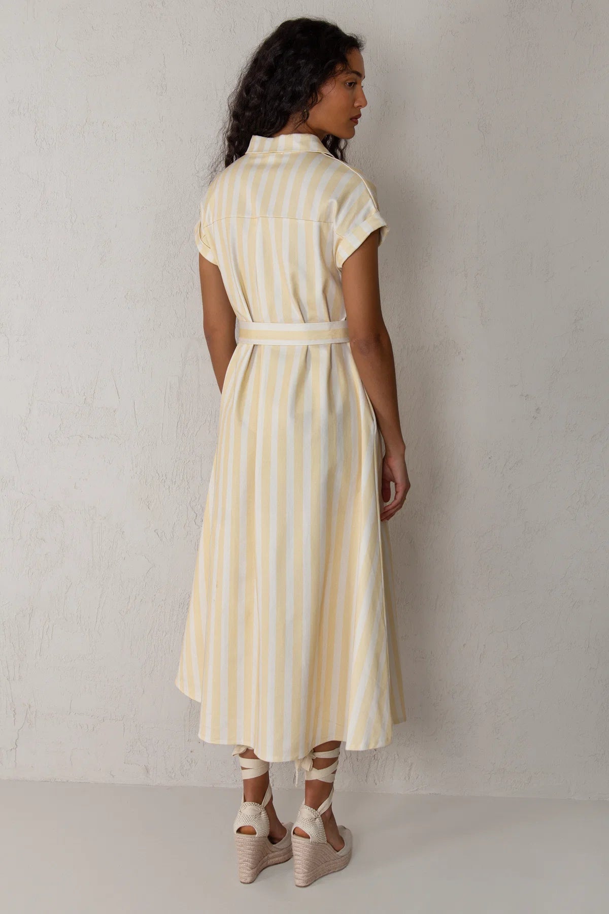 Woman wearing a yellow and white striped dress against a plain background