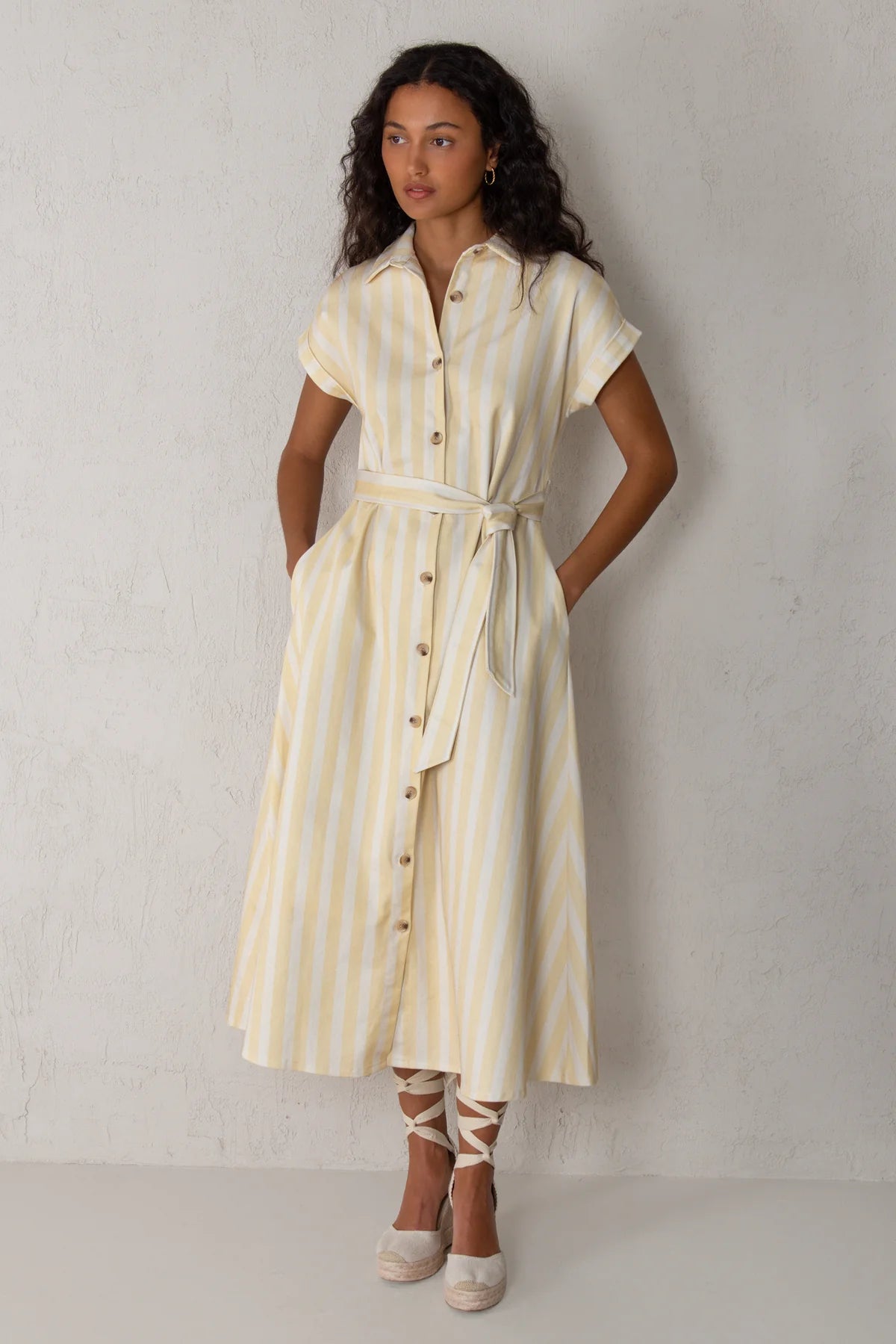 woman wearing yellow and cream striped dress with pockets on a beige background