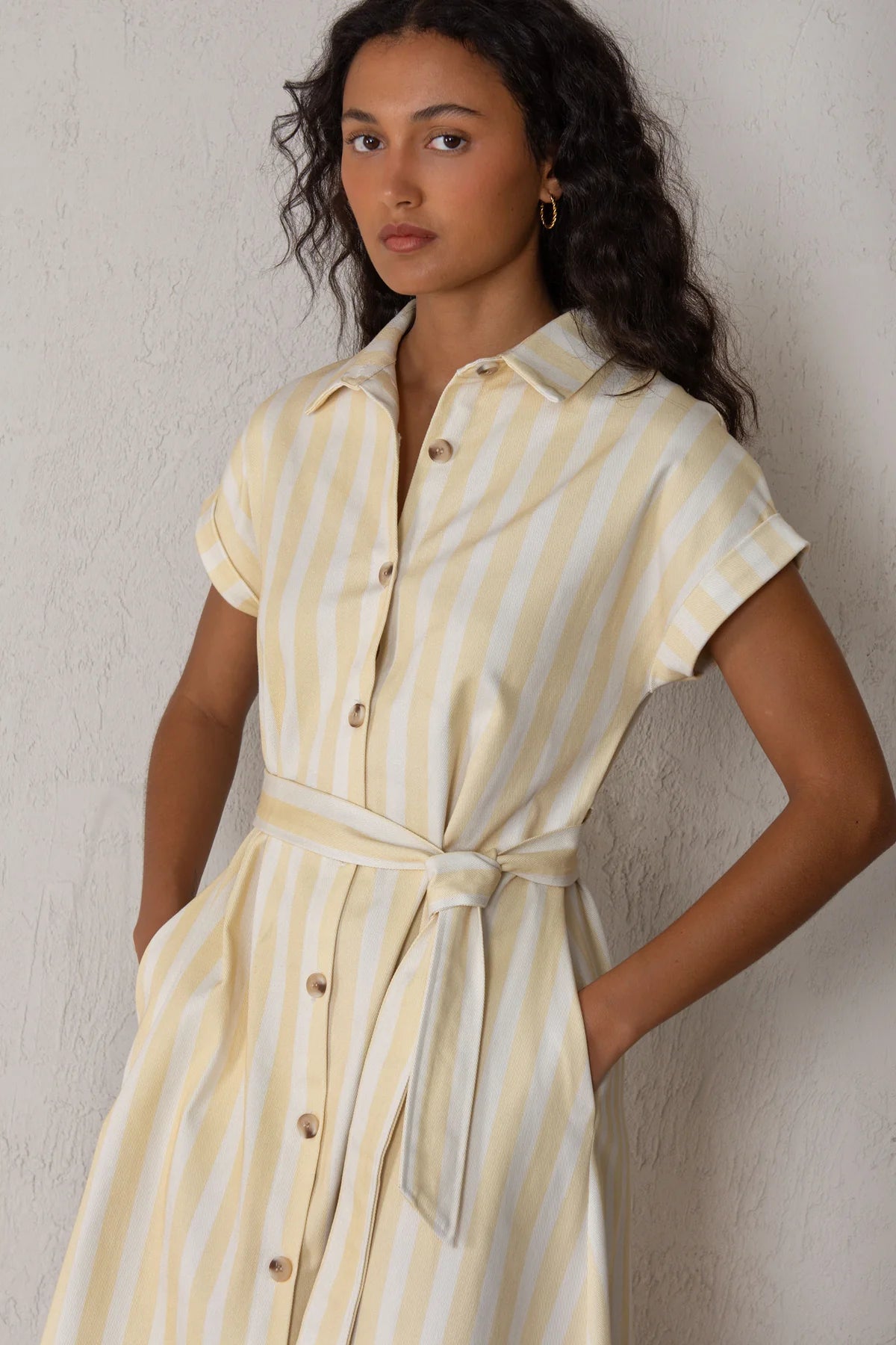 Woman wearing a yellow and white striped dress against a neutral background