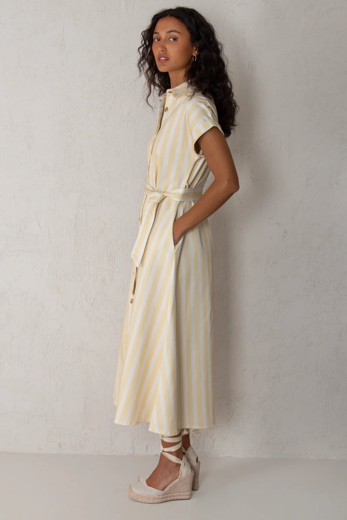 Woman wearing a yellow and white striped dress against a plain background